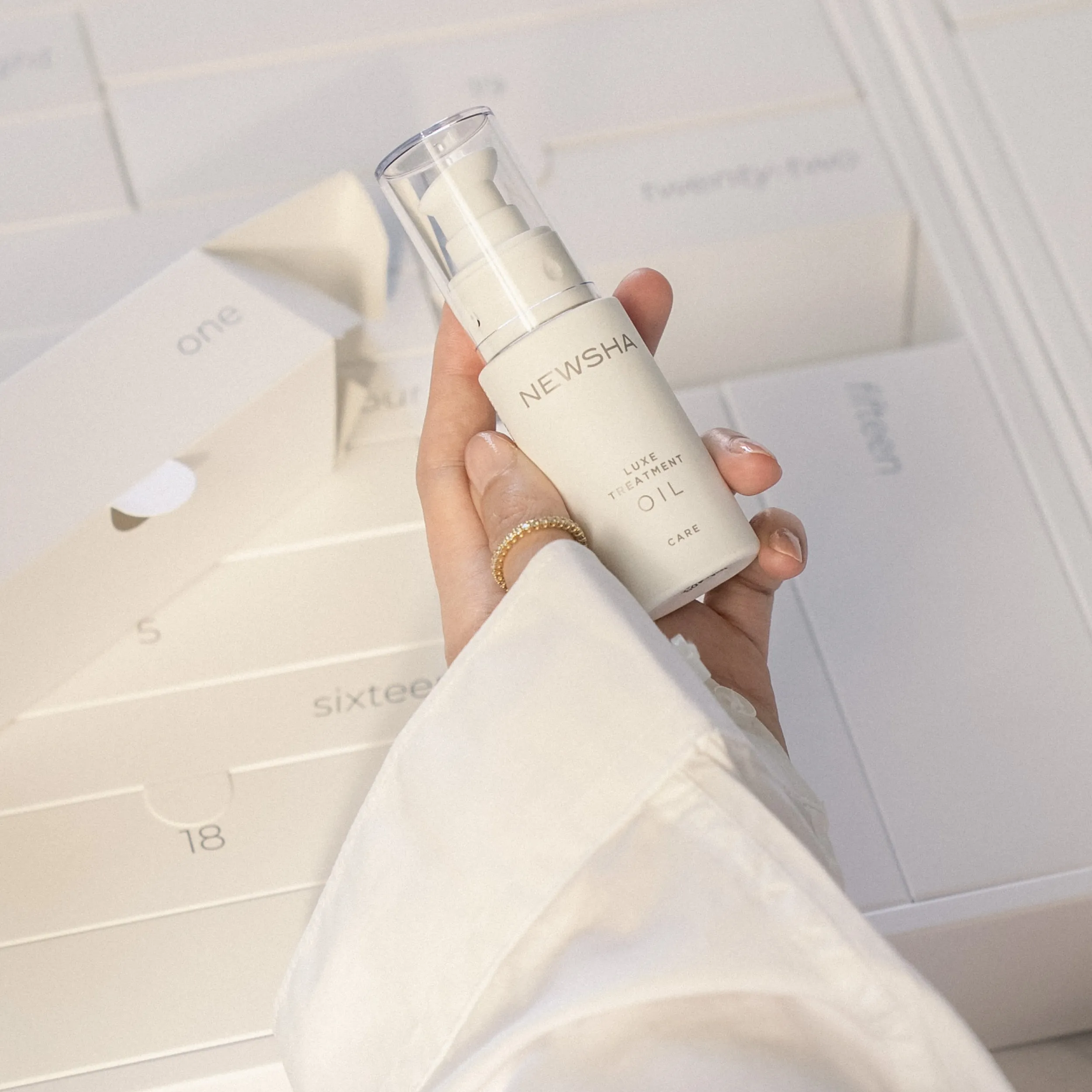 Hand h&auml;lt das NEWSHA Luxe Treatment Oil &uuml;ber einem ge&ouml;ffneten NEWSHA Adventskalender mit nummerierten F&auml;chern.